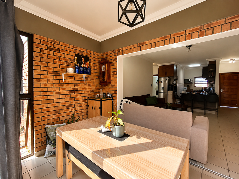 Open-plan living and dining area featuring an exposed brick feature wall, tiled flooring, and a seamless flow into the adjacent kitchen space.
