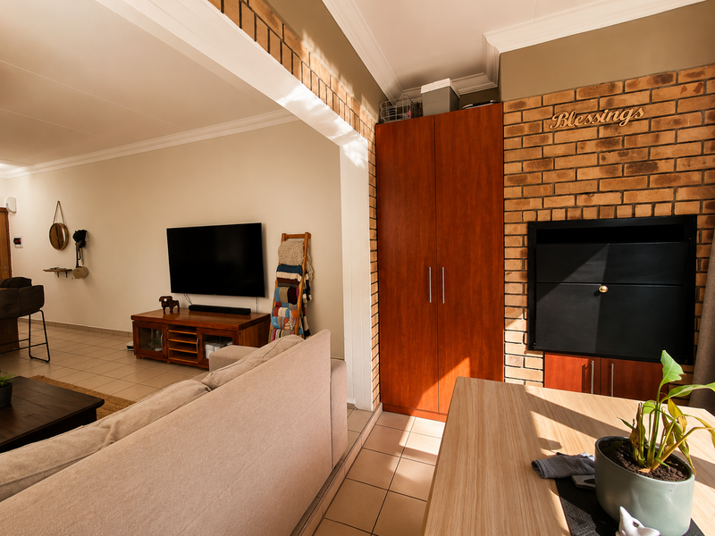 Open plan living area featuring tiled floors, a built-in fireplace with an exposed brick surround, and integrated storage cabinetry.