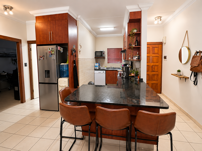 Open-plan kitchen featuring dark wood cabinetry, granite countertops, a breakfast bar, and tiled flooring, seamlessly connecting to the adjacent living area.