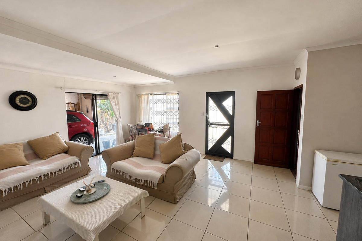 A bright living room featuring large format floor tiles, a coved ceiling, and direct access to the exterior through a sliding glass door.