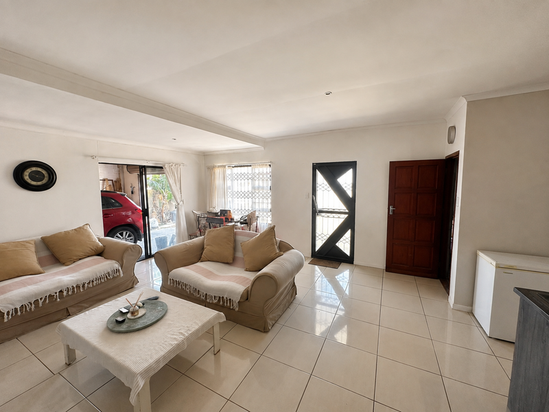 A bright living room featuring large format floor tiles, a coved ceiling, and direct access to the exterior through a sliding glass door.