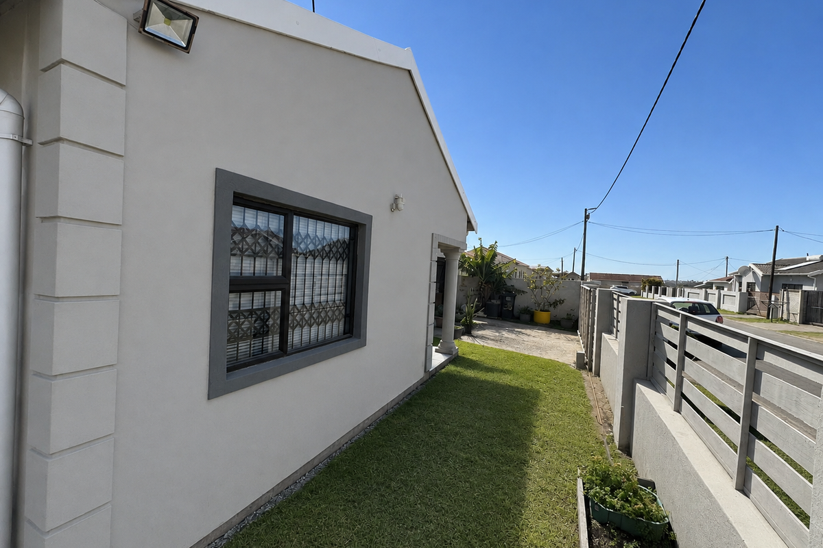 Side exterior view of the property featuring a well-maintained lawn, boundary wall with metal fencing, and security lighting.