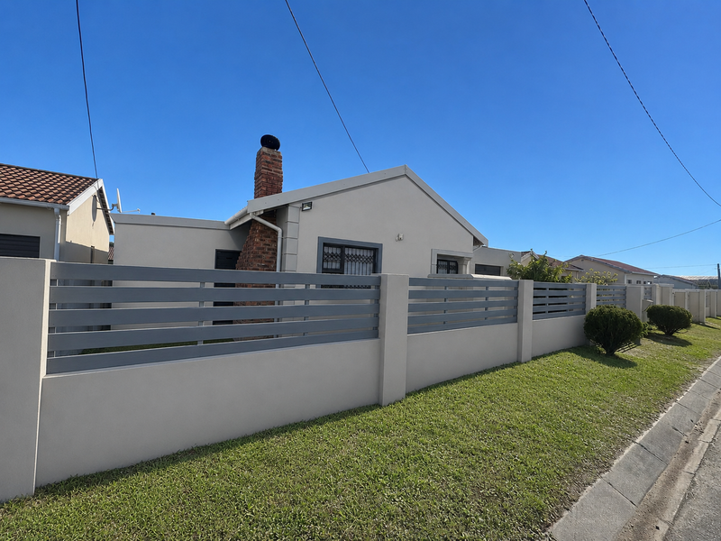 Front view of a well-maintained house featuring a brick chimney, modern slatted perimeter fencing, and a neat lawn.