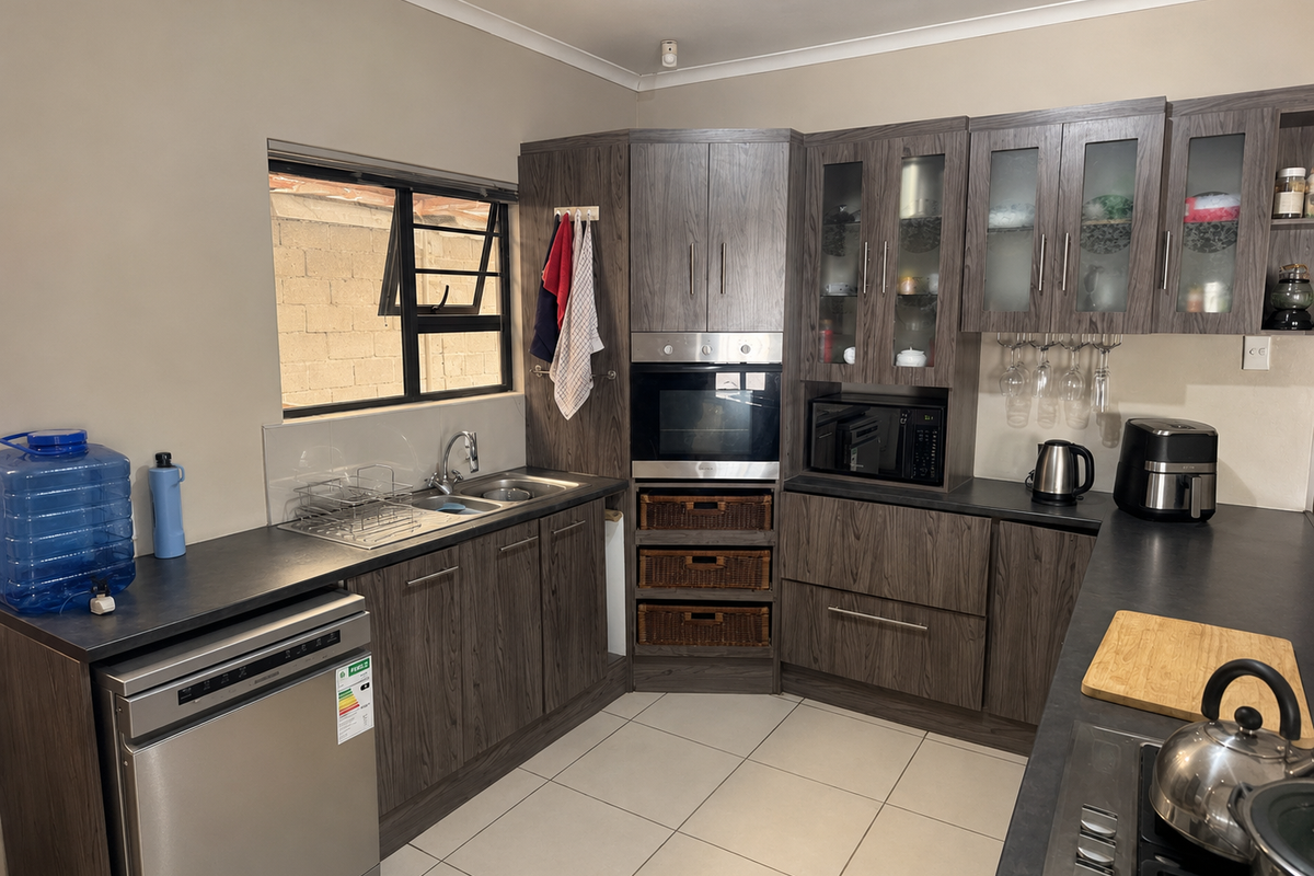 A functional kitchen featuring dark wood-grain cabinetry, integrated oven and microwave, stainless steel sink, and tiled flooring with ample counter space.