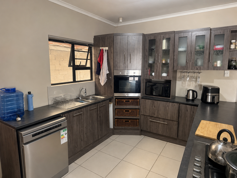 A functional kitchen featuring dark wood-grain cabinetry, integrated oven and microwave, stainless steel sink, and tiled flooring with ample counter space.
