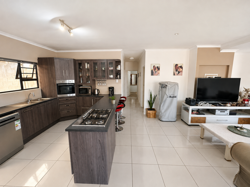 Spacious open-plan living area featuring a modern kitchen with dark wood cabinetry, integrated oven, gas cooktop, and sleek tiled flooring throughout.