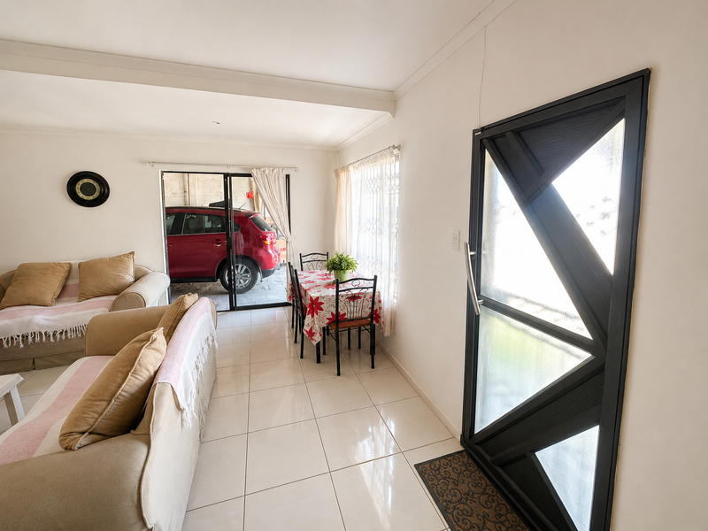 Open plan living and dining area featuring tiled flooring, a modern security entrance door, and large windows with security bars.