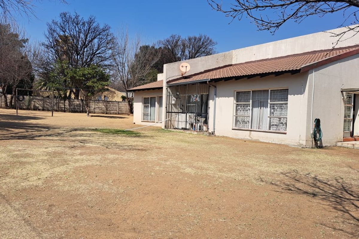 Rear view of the house featuring a tiled roof, security bars on windows, and a large, dry garden area with boundary walling.