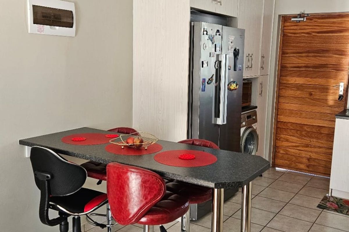 Compact kitchen area featuring light-toned built-in cabinetry, tiled flooring, and a breakfast bar, providing a functional space with direct access to the main entrance.