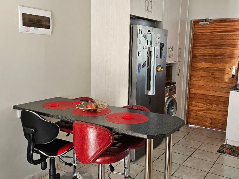 Compact kitchen area featuring light-toned built-in cabinetry, tiled flooring, and a breakfast bar, providing a functional space with direct access to the main entrance.