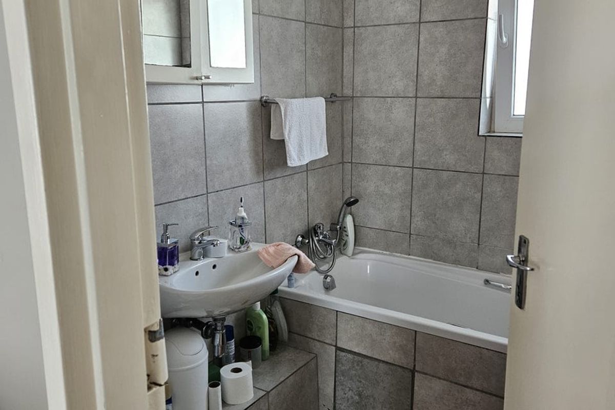 A compact bathroom featuring a bathtub, pedestal basin, and toilet, finished with neutral grey wall and floor tiles.