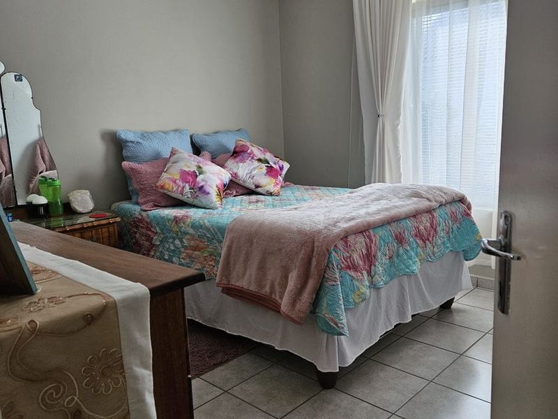 A functional bedroom featuring neutral wall paint, tiled flooring, and a window with curtain tracks, offering a clean and simple living space.