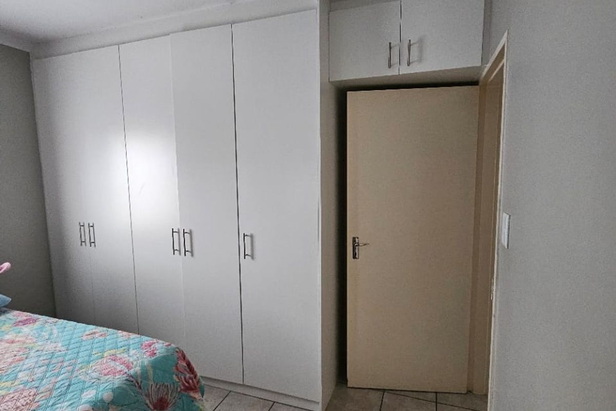 Bedroom featuring built-in white cupboards with overhead storage, tiled flooring, and neutral wall finishes.
