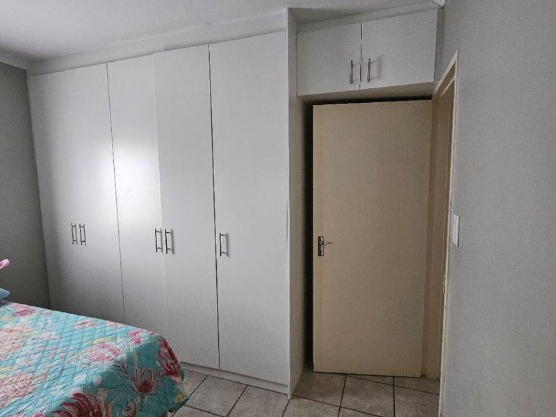 Bedroom featuring built-in white cupboards with overhead storage, tiled flooring, and neutral wall finishes.