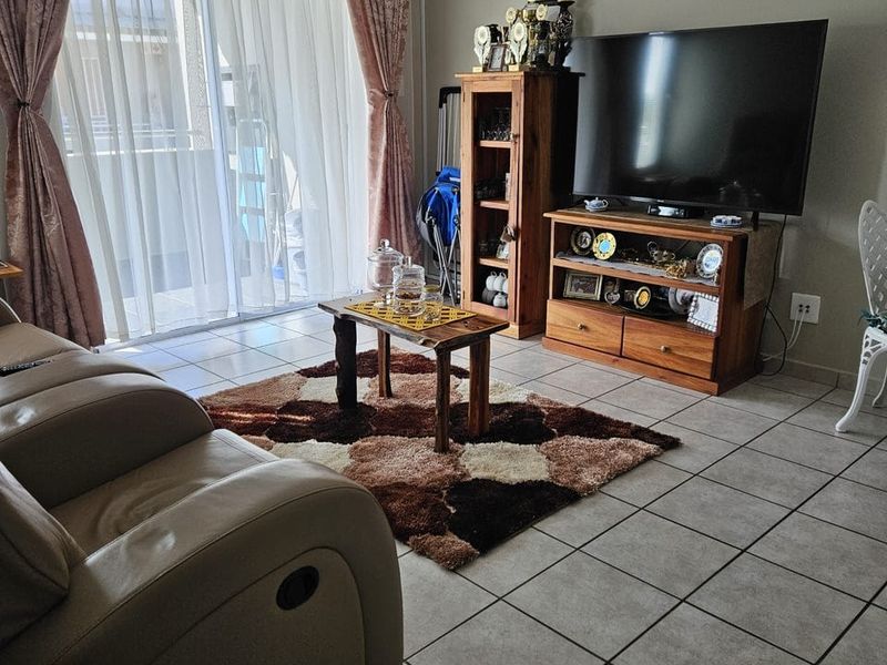 A living room featuring neutral tiled flooring and a large sliding glass door providing access to an outdoor balcony area.