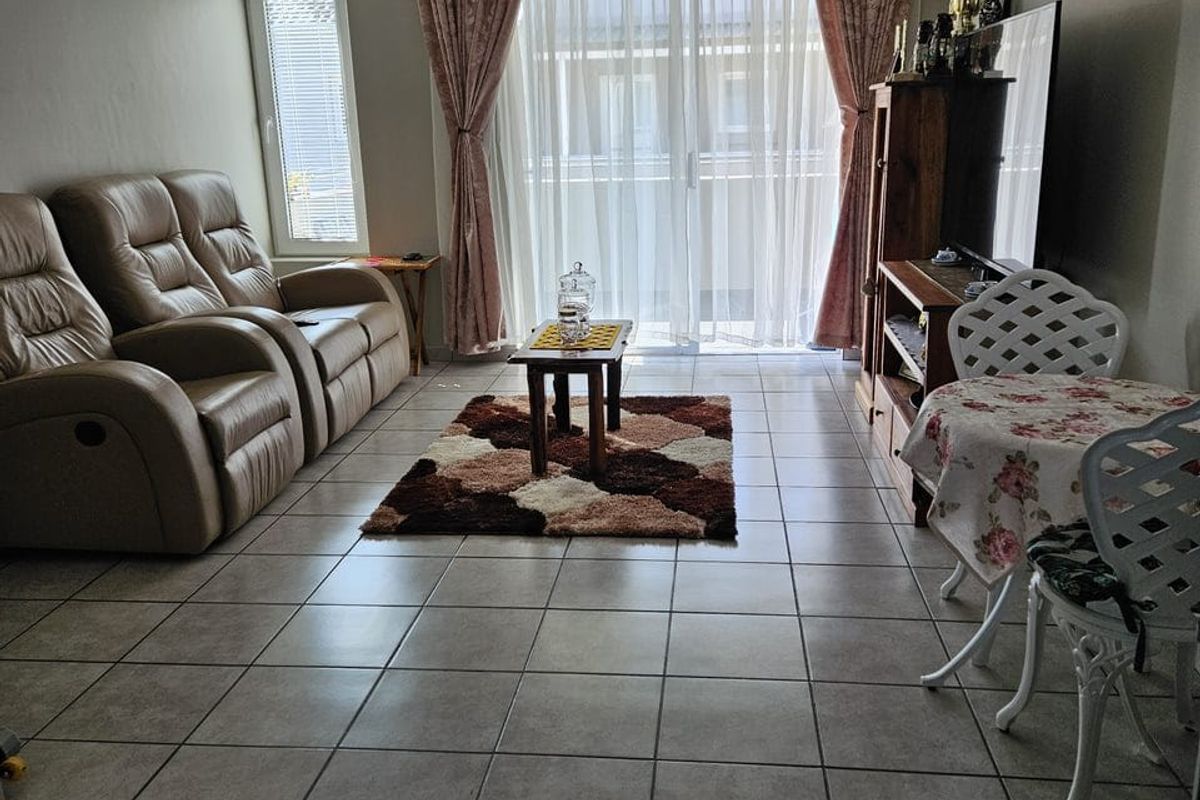 A living room featuring neutral tiled flooring, a sliding glass door leading to an outdoor area, and a casement window.