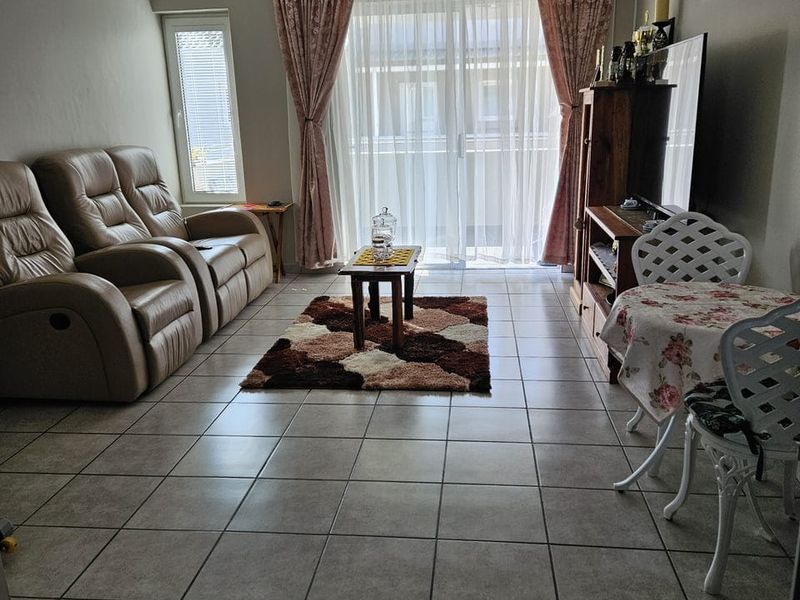 A living room featuring neutral tiled flooring, a sliding glass door leading to an outdoor area, and a casement window.
