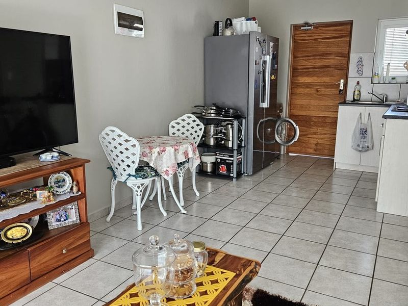 Open-plan living area featuring tiled flooring, a compact kitchen corner with cabinetry and sink, and direct access to a wooden entrance door.