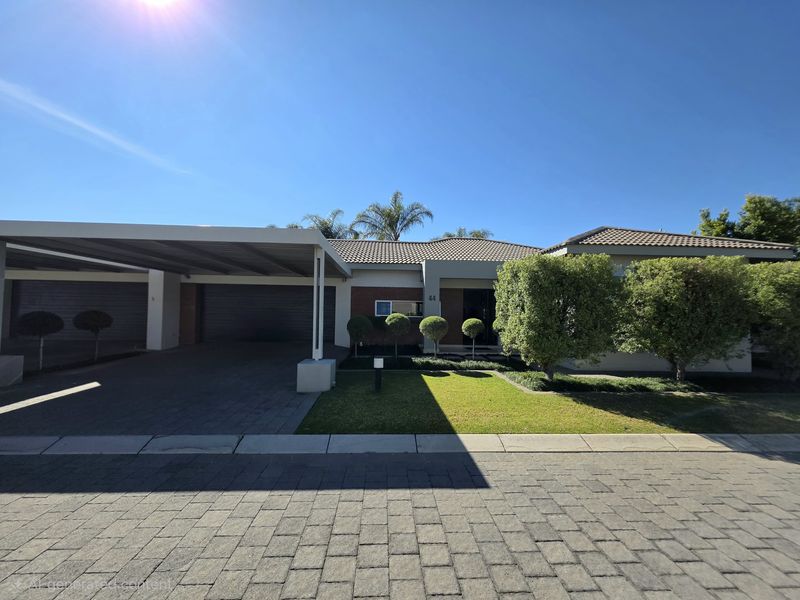 A well-maintained townhouse exterior featuring a spacious carport, paved driveway, and neat front garden with established landscaping.