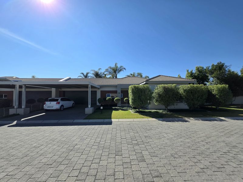 Front exterior view of the townhouse featuring a paved driveway, covered carport, and well-maintained landscaped garden area.