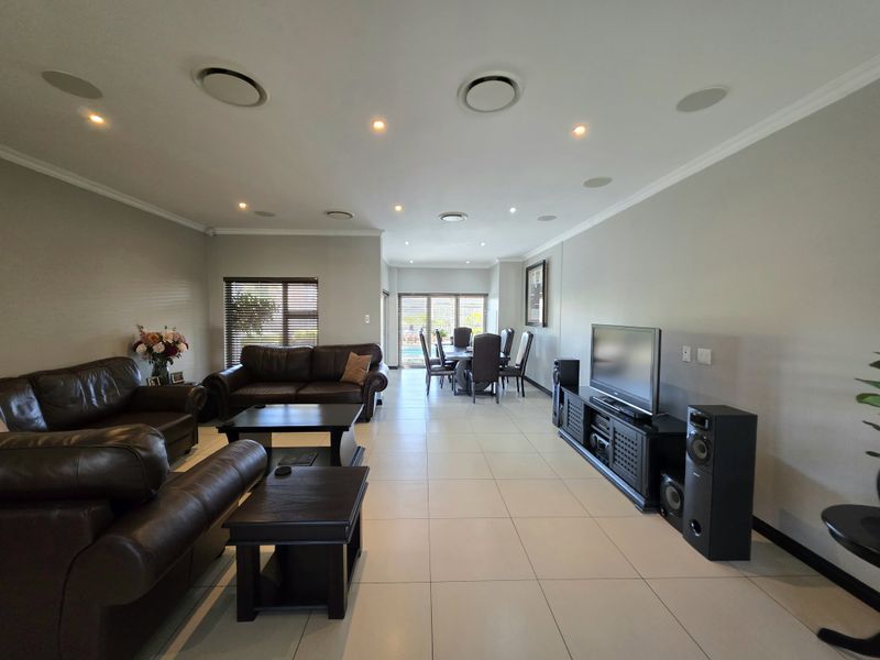 Spacious open-plan living and dining area featuring neutral tiled flooring, recessed downlighting, integrated ceiling speakers, and large sliding doors leading to the outdoor space.