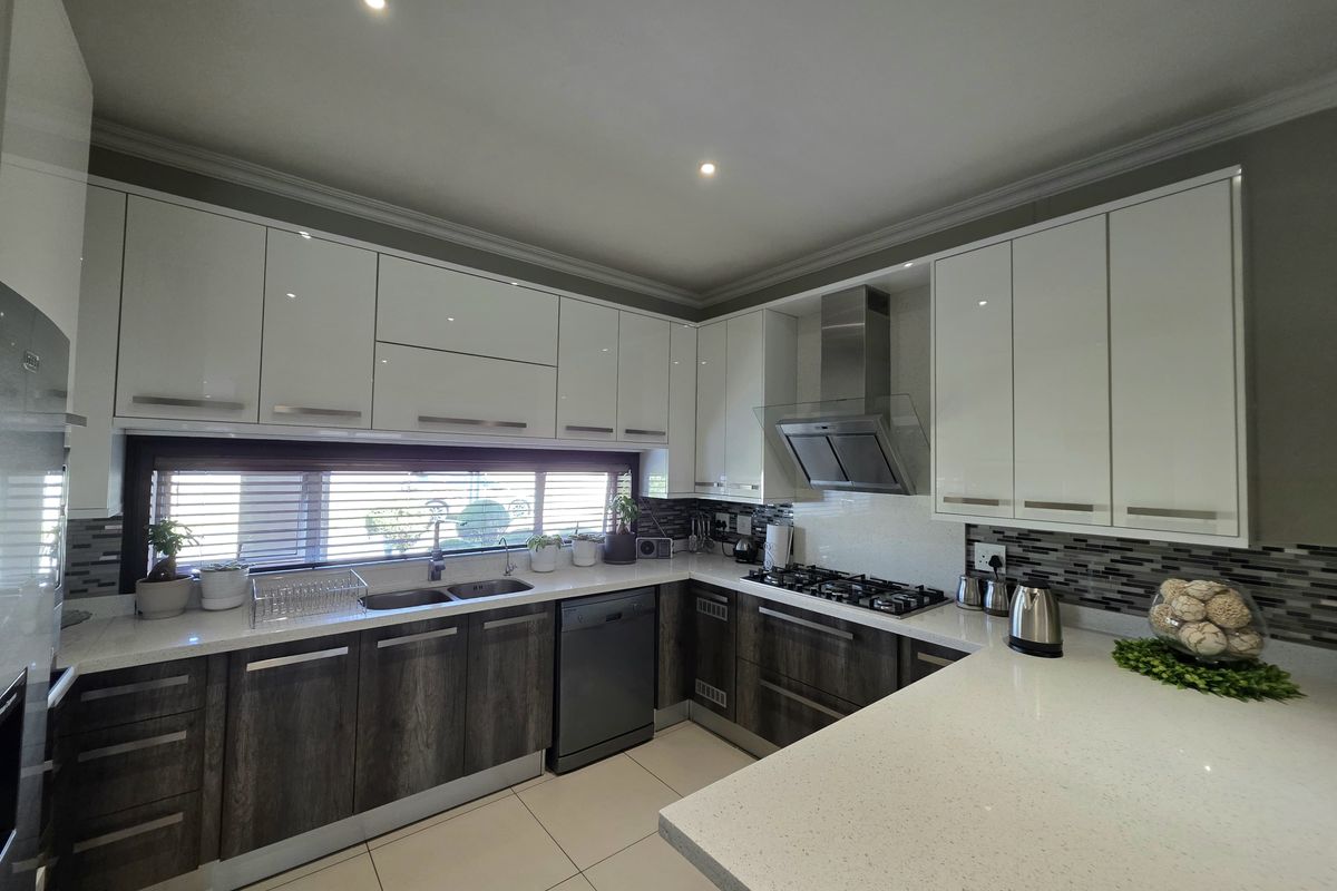 Modern kitchen featuring high-gloss white upper cabinets, dark wood-grain lower cabinetry, quartz countertops, gas hob, and integrated stainless steel appliances.