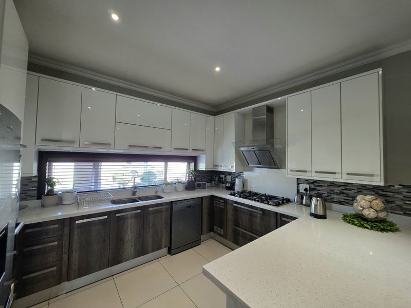 Modern kitchen featuring high-gloss white upper cabinets, dark wood-grain lower cabinetry, quartz countertops, gas hob, and integrated stainless steel appliances.