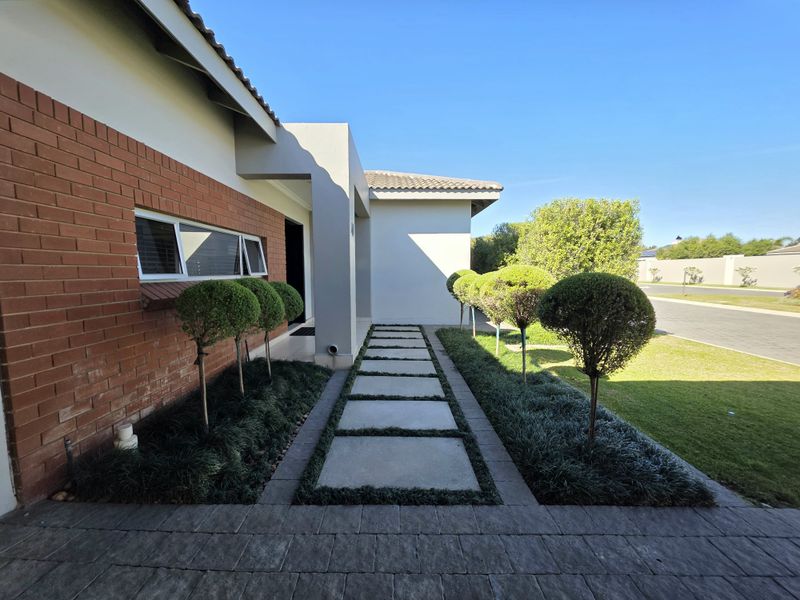 A well-maintained front entrance featuring a brick facade, a paved walkway, and manicured garden beds leading to the main doorway.