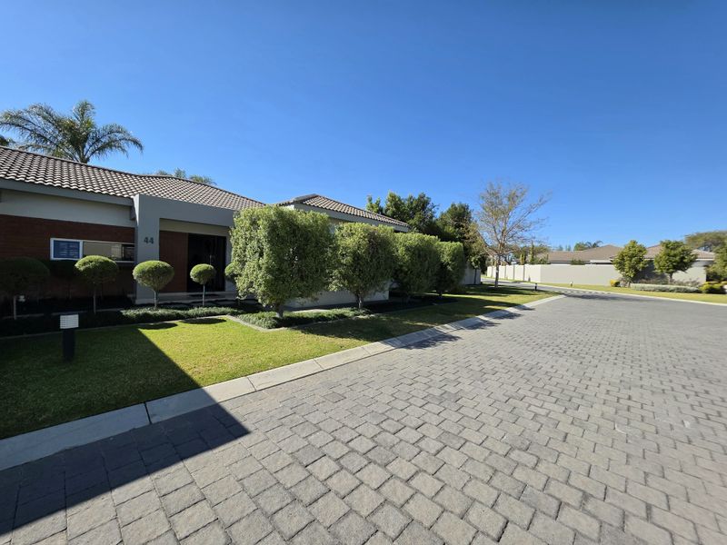 Front elevation of a well-maintained townhouse featuring a brick facade, tiled roof, and a neat paved driveway with landscaped garden borders.