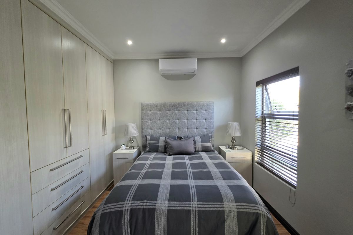A well-maintained bedroom featuring extensive built-in cabinetry, laminate flooring, recessed lighting, and a wall-mounted air conditioning unit.