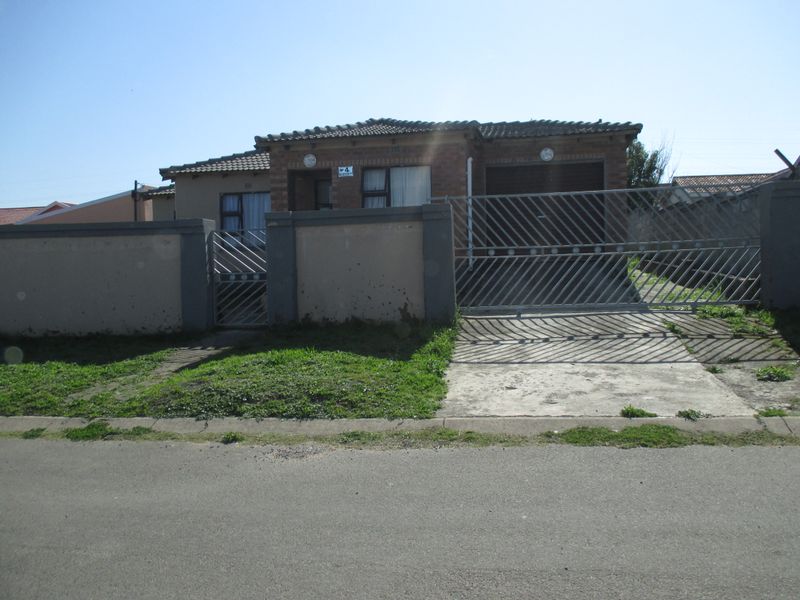 Front view of a single-story brick house featuring a perimeter wall, metal driveway gate, and attached garage.
