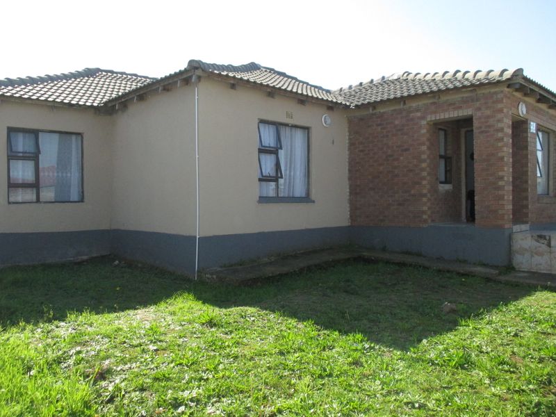 Rear view of a single-story residential house featuring a combination of plastered and brick exterior walls with tiled roofing and casement windows.