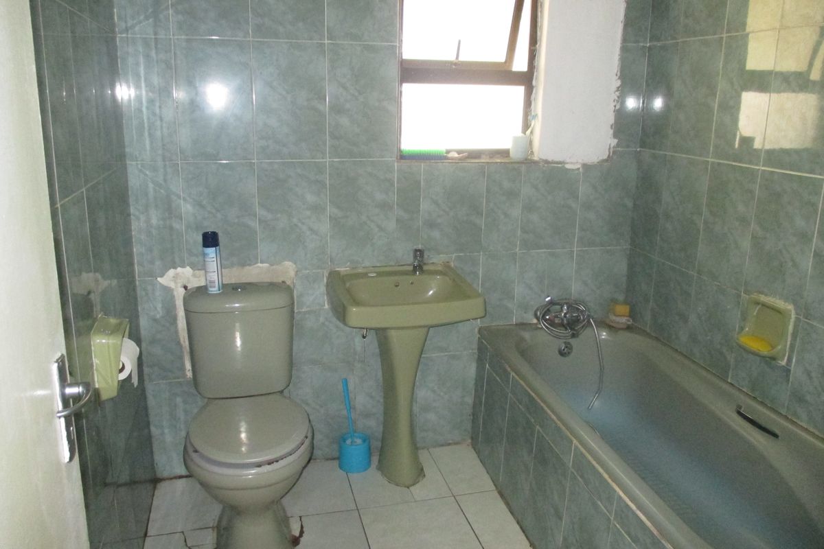 A dated bathroom featuring a pedestal basin, toilet, and bathtub with green wall tiling. The space requires renovation and repair to modern standards.