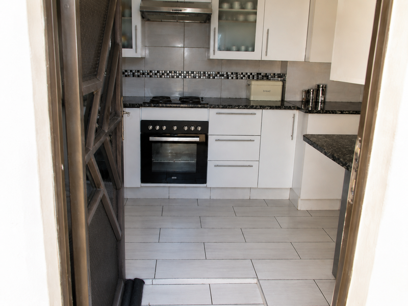 A functional kitchen featuring white cabinetry, granite countertops, a built-in oven with hob, extractor fan, and neutral tiled flooring.