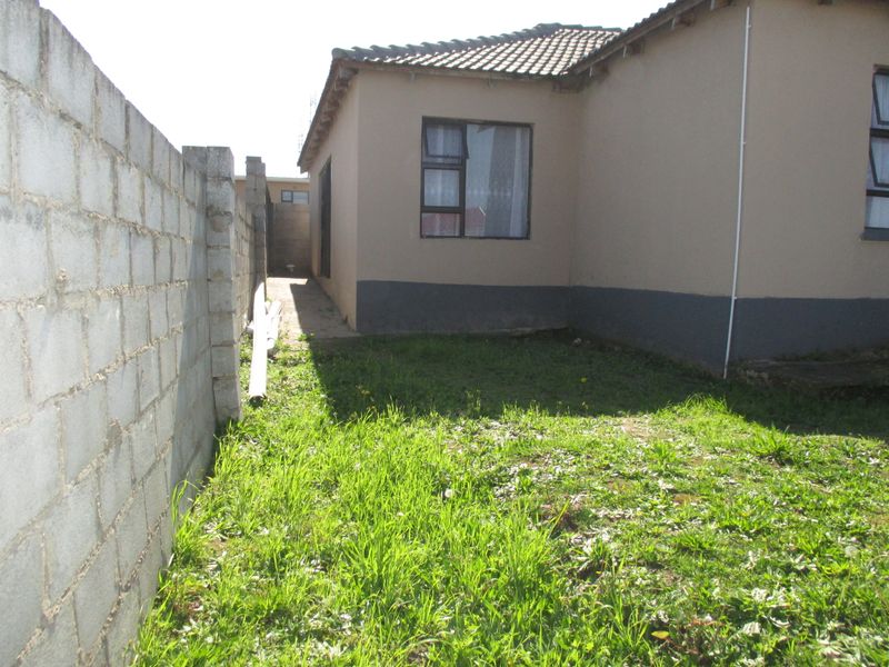 A view of the rear exterior of the house featuring a concrete block boundary wall and a small grassed yard area.