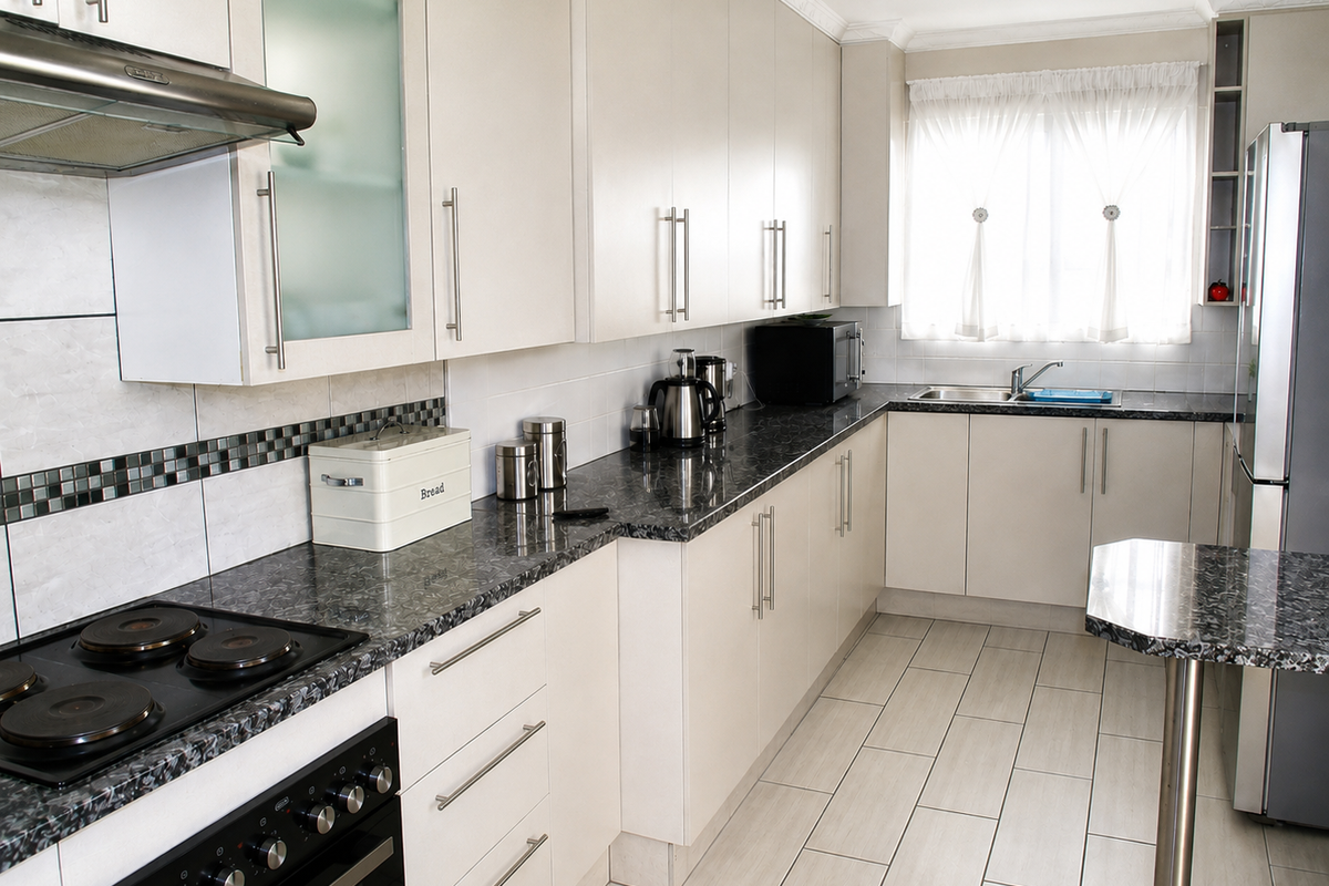 A well-maintained kitchen featuring light-toned cabinetry, dark granite countertops, a built-in electric stove with extractor fan, and neutral tiled flooring.