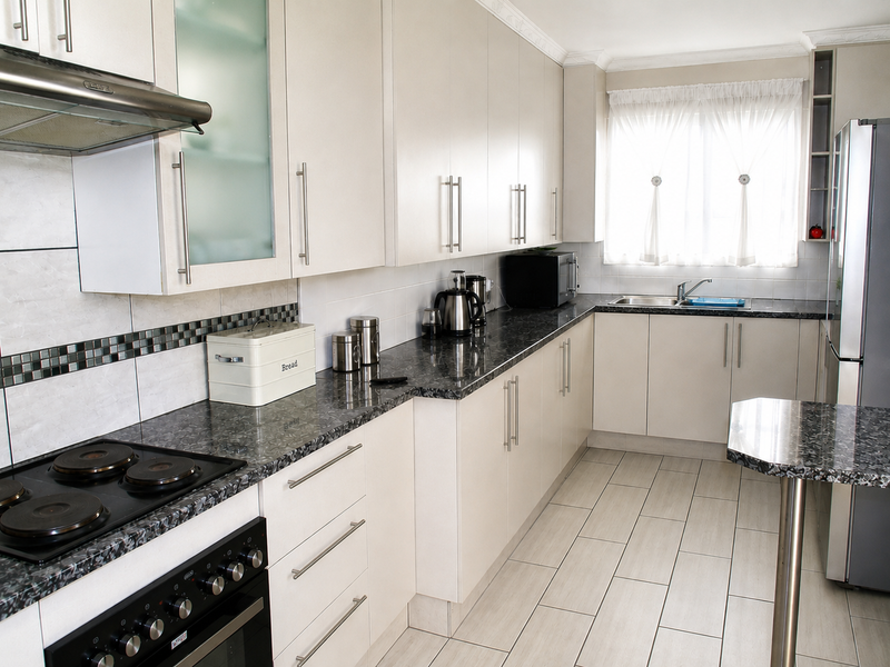 A well-maintained kitchen featuring light-toned cabinetry, dark granite countertops, a built-in electric stove with extractor fan, and neutral tiled flooring.