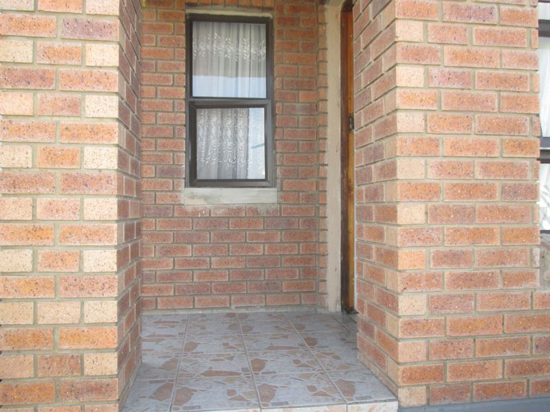 A simple entrance area featuring face brick walls and tiled flooring, providing a functional and classic exterior access point to the home.