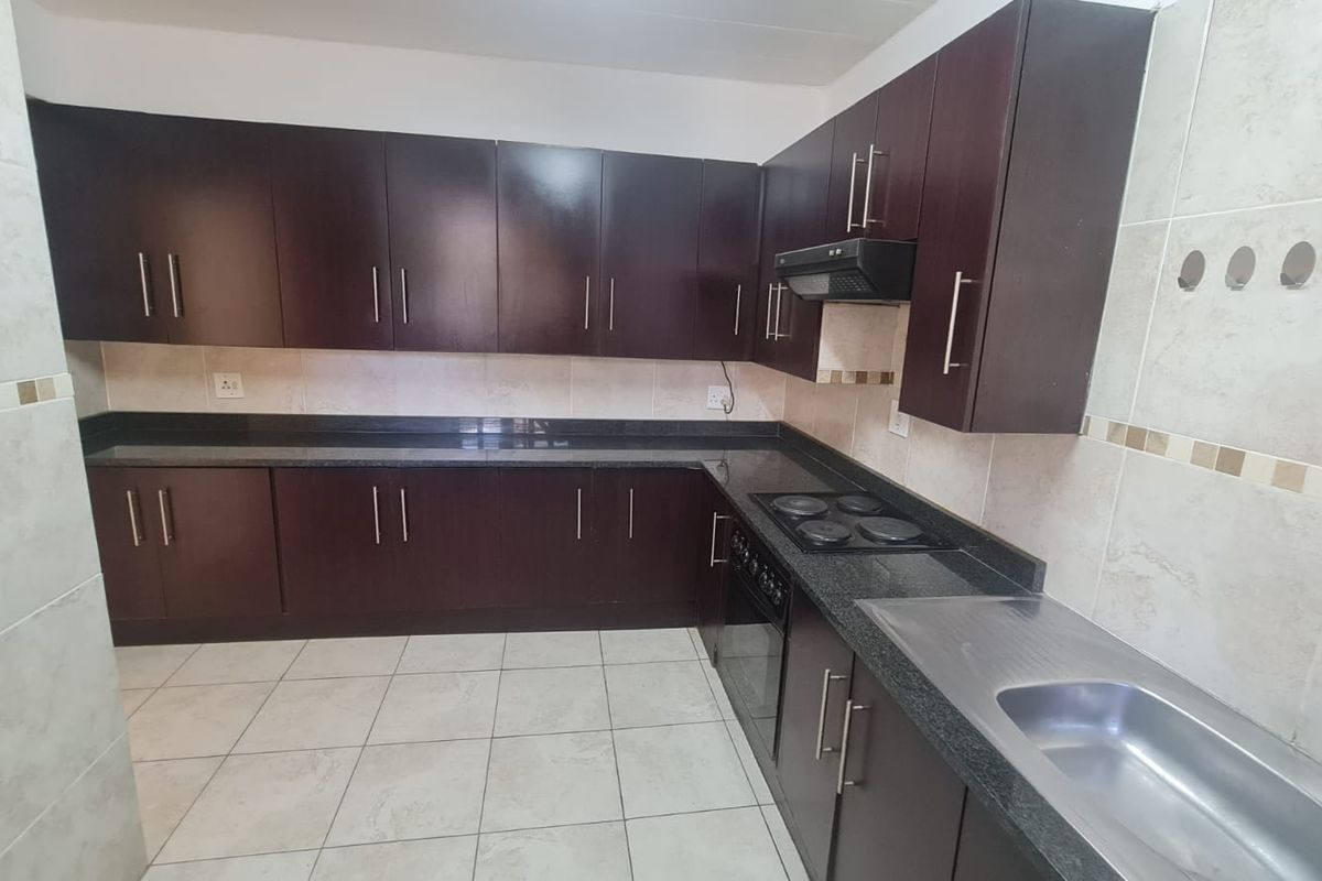 A clean, functional kitchen featuring dark wood cabinetry, granite countertops, built-in oven, electric hob, and tiled finishes throughout.