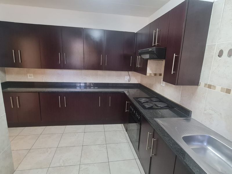 A clean, functional kitchen featuring dark wood cabinetry, granite countertops, built-in oven, electric hob, and tiled finishes throughout.