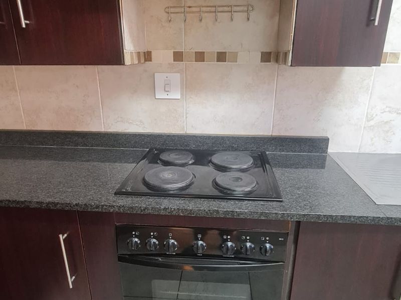 A functional kitchen area featuring dark wood cabinetry, granite countertops, a built-in electric oven, hob, and extractor fan with tiled backsplash.