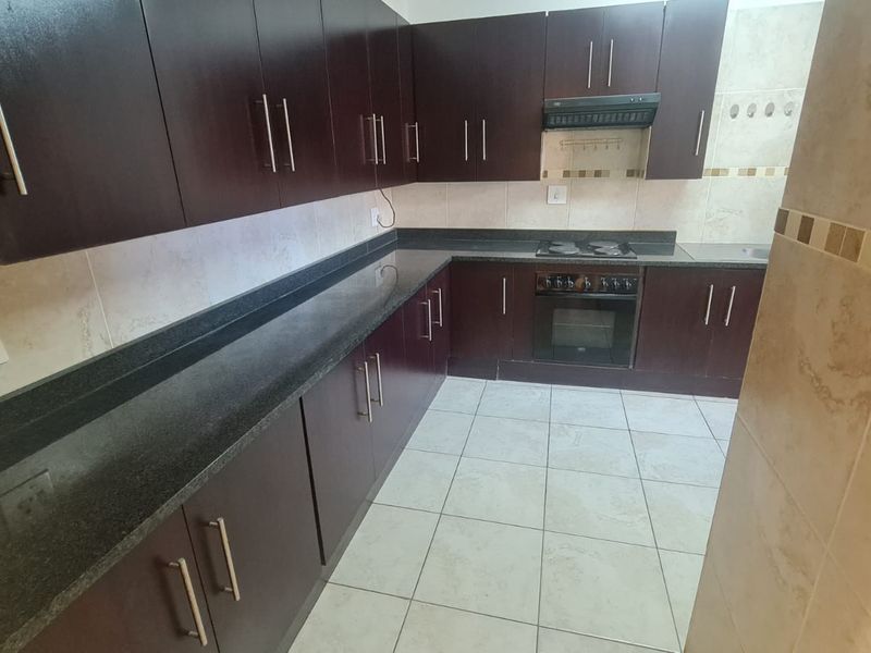 A clean, functional kitchen featuring dark wood cabinetry, granite countertops, built-in oven, electric hob, and neutral tiled flooring.