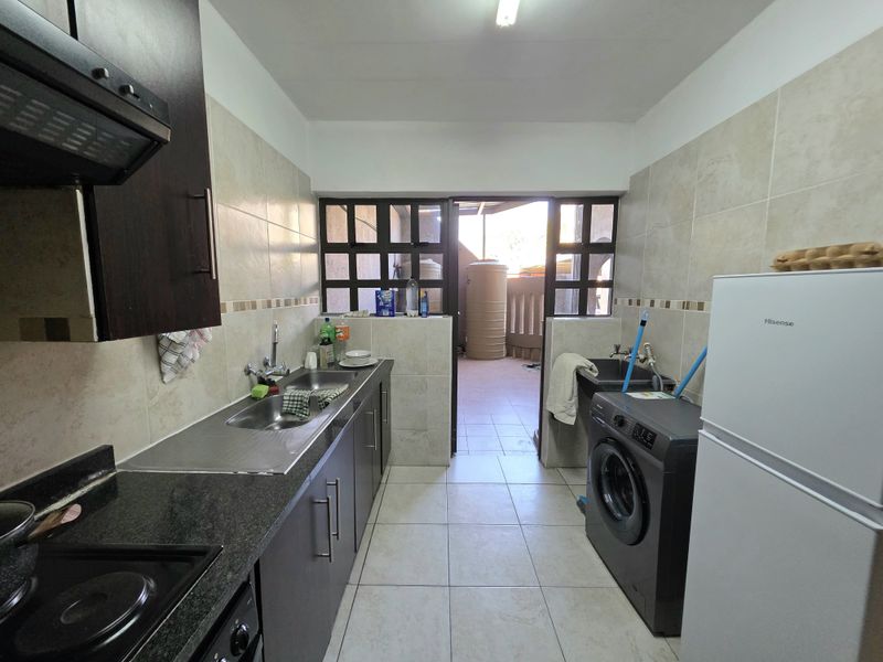 A functional kitchen featuring dark cabinetry, granite countertops, tiled finishes, and integrated laundry plumbing, with direct access to an outdoor area.