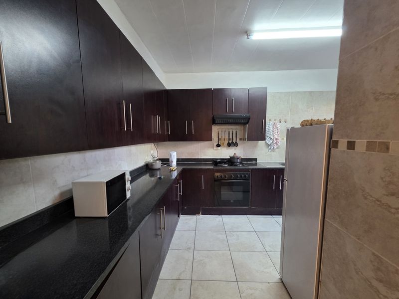 A functional kitchen featuring dark wood cabinetry, granite countertops, a built-in oven with gas hob, and tiled flooring throughout.