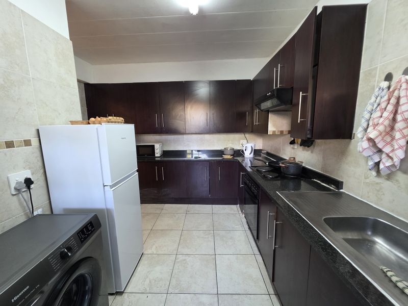A functional kitchen featuring dark wood cabinetry, granite countertops, a built-in oven with hob, and tiled finishes throughout.