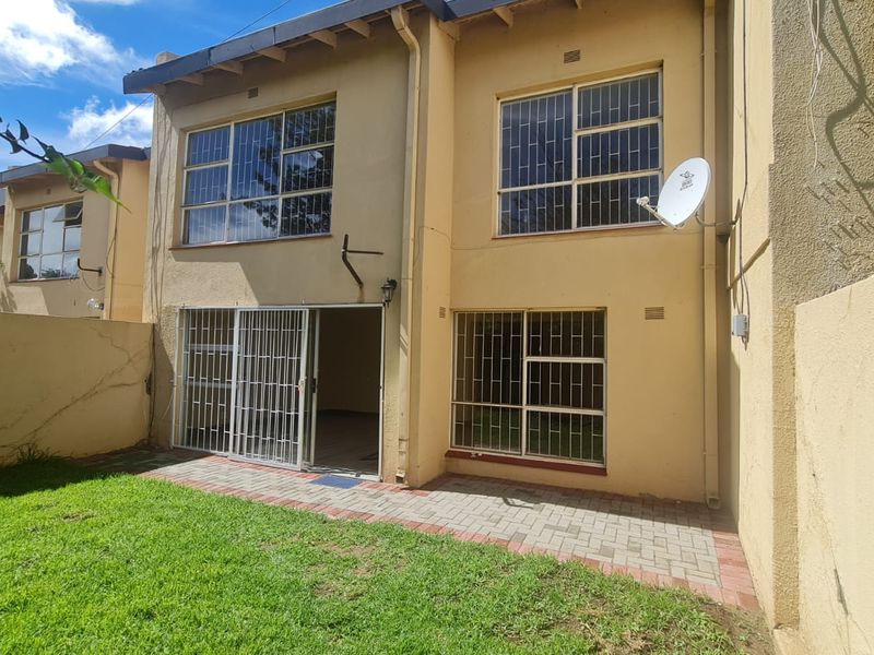 Rear view of the property featuring a paved patio area, small lawn, and security bars on windows and sliding doors.