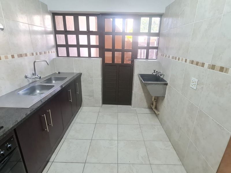 A functional scullery featuring tiled walls and floors, double stainless steel sink, additional utility sink, and built-in cabinetry with integrated oven and hob.