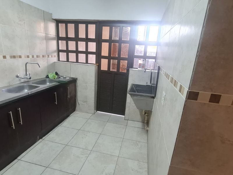A functional scullery area featuring dark wood cabinetry, double stainless steel sink, additional utility sink, and tiled finishes throughout.