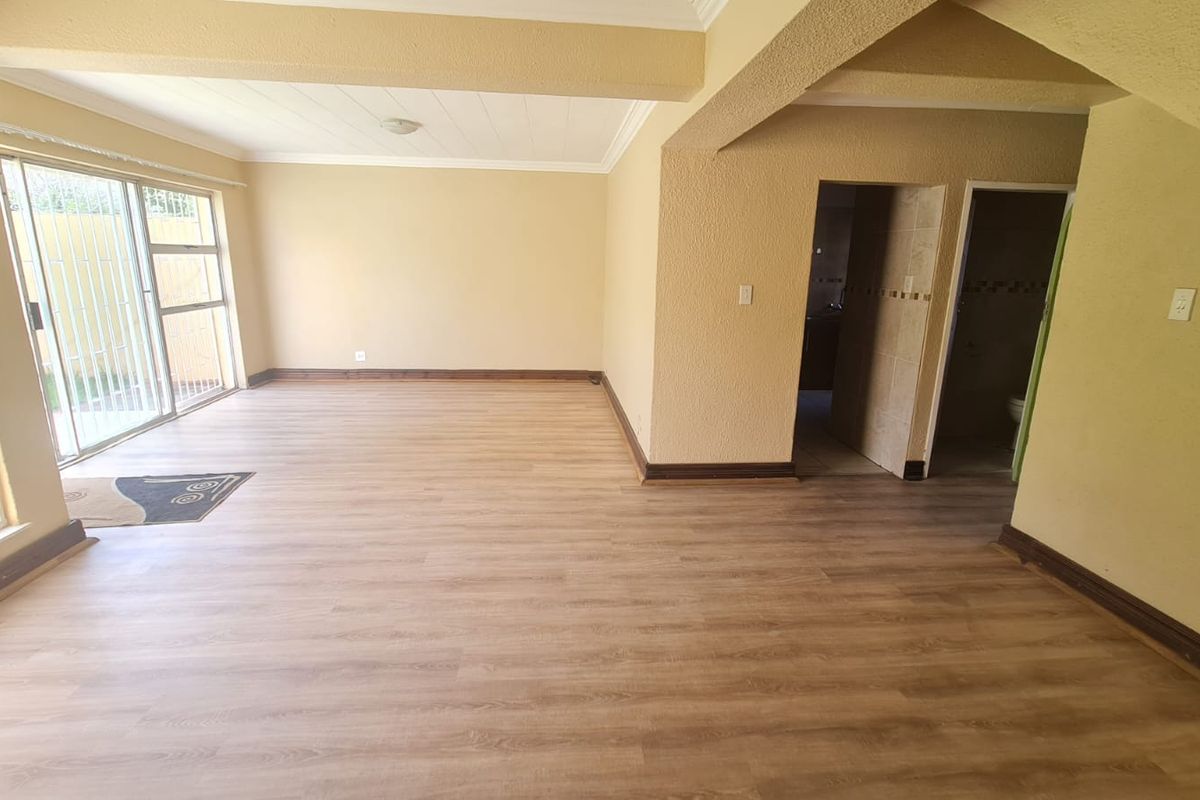 Spacious, empty living area featuring light wood-look laminate flooring, textured walls, and a sliding glass door with security bars leading to the exterior.