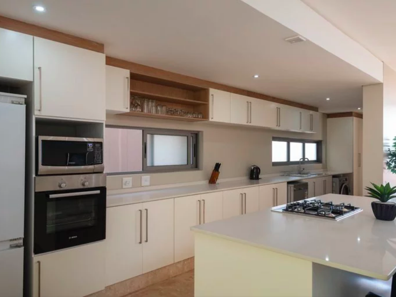 Modern kitchen featuring sleek white cabinetry, stone countertops, a central island with a gas cooktop, and integrated appliances.